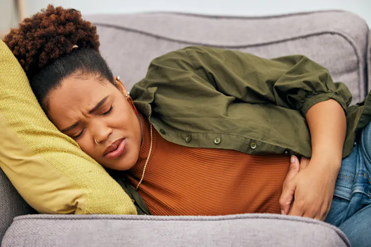 A woman lies on the couch in pain.