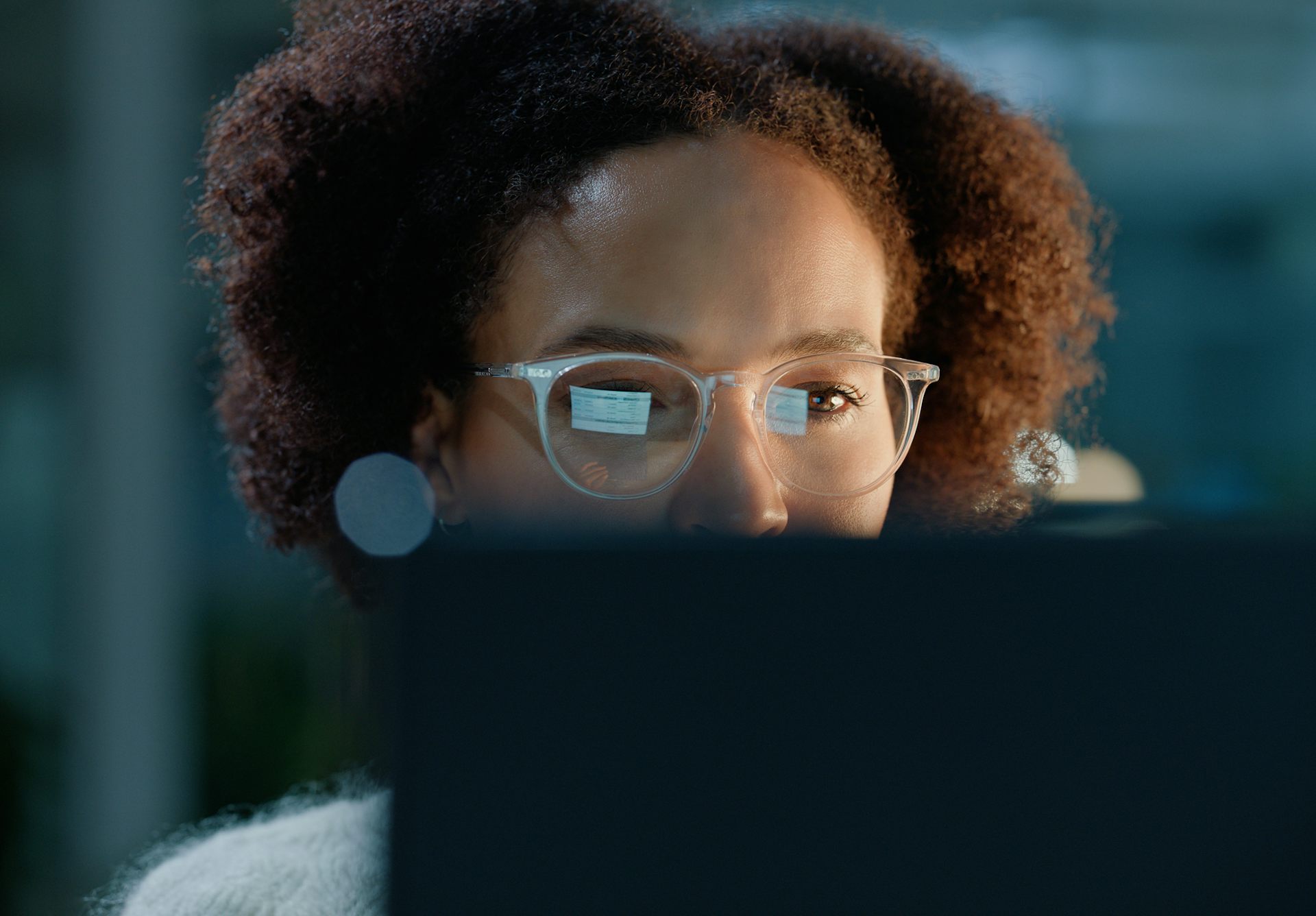 A woman wearing spectacles looks at a computer screen, whose image is reflected in the lenses