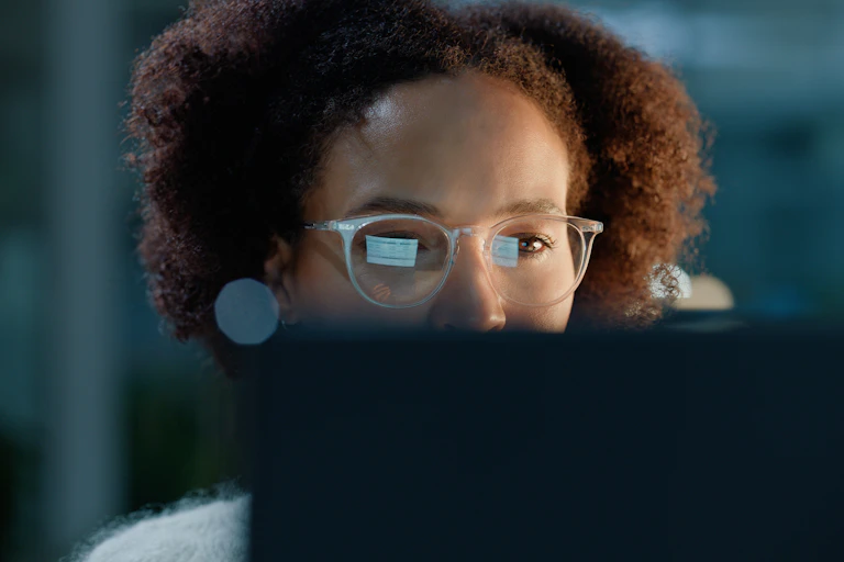 A woman wearing spectacles looks at a computer screen, whose image is reflected in the lenses
