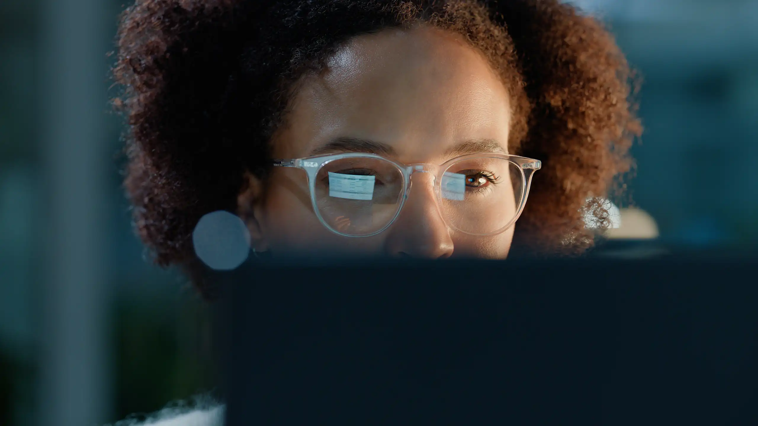 A woman wearing spectacles looks at a computer screen, whose image is reflected in the lenses