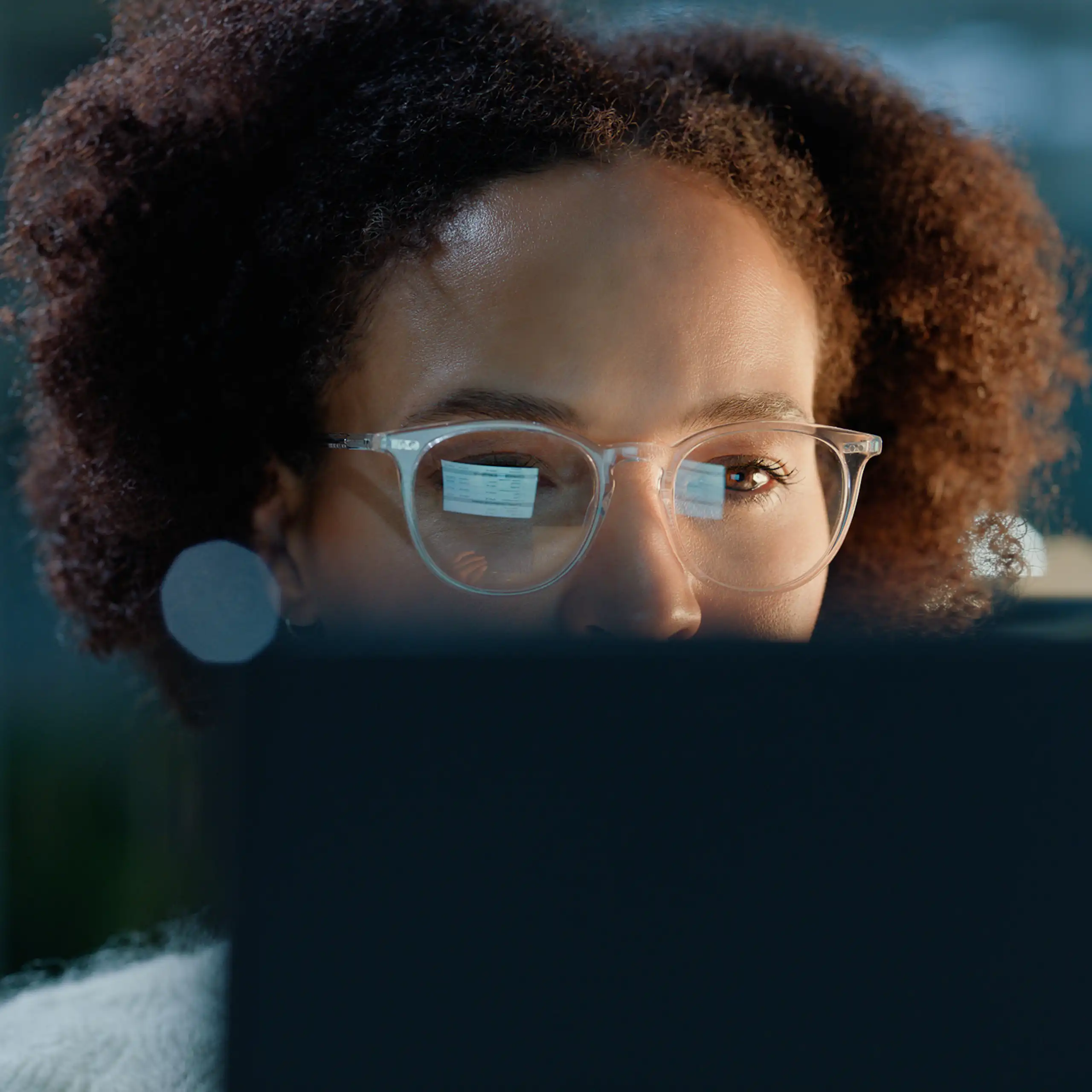 A woman wearing spectacles looks at a computer screen, whose image is reflected in the lenses