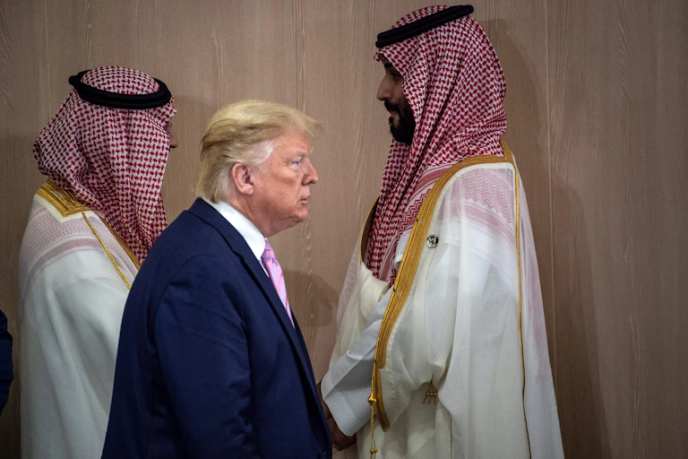A man in a suit walks past two men in traditional Persian Gulf dress.