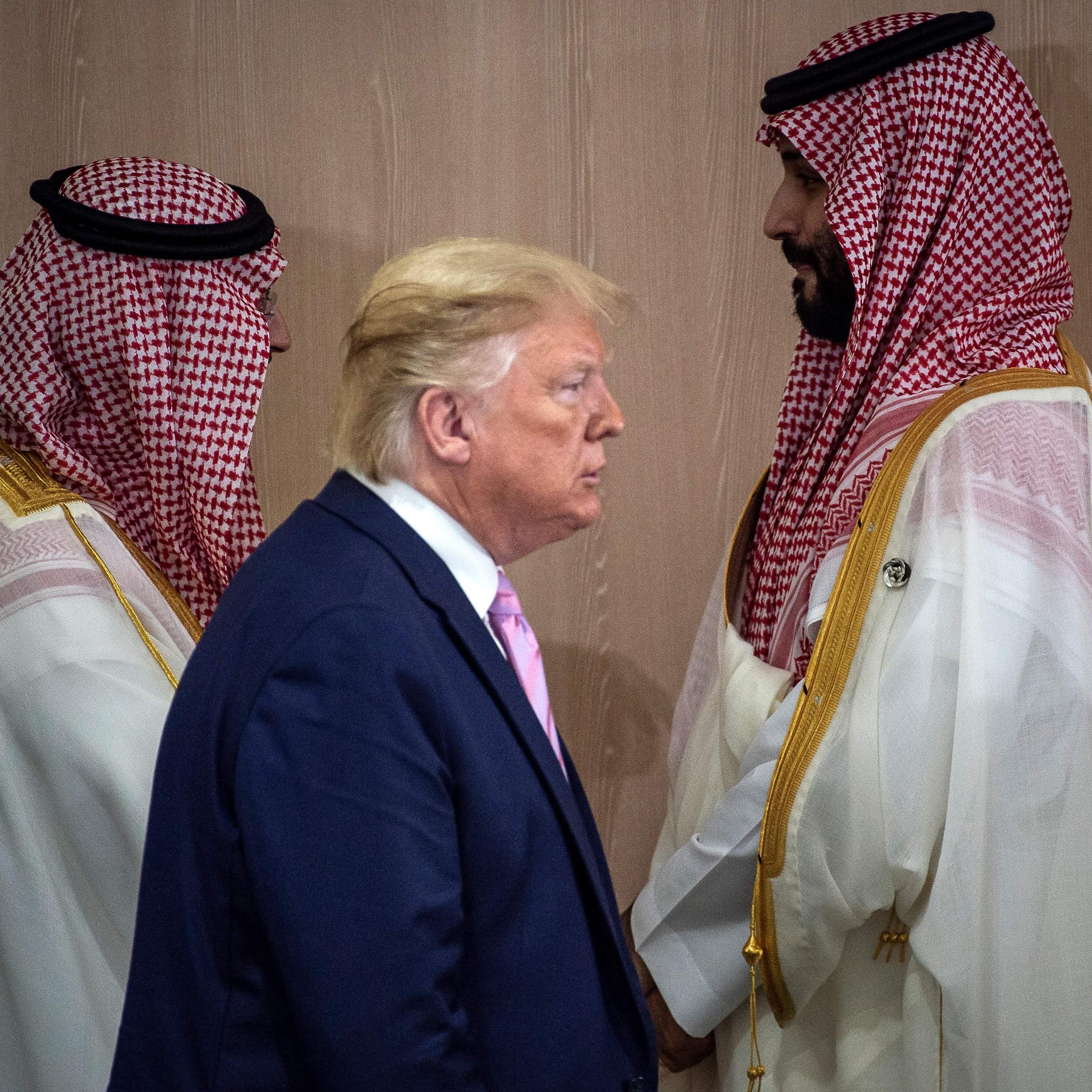 A man in a suit walks past two men in traditional Persian Gulf dress.