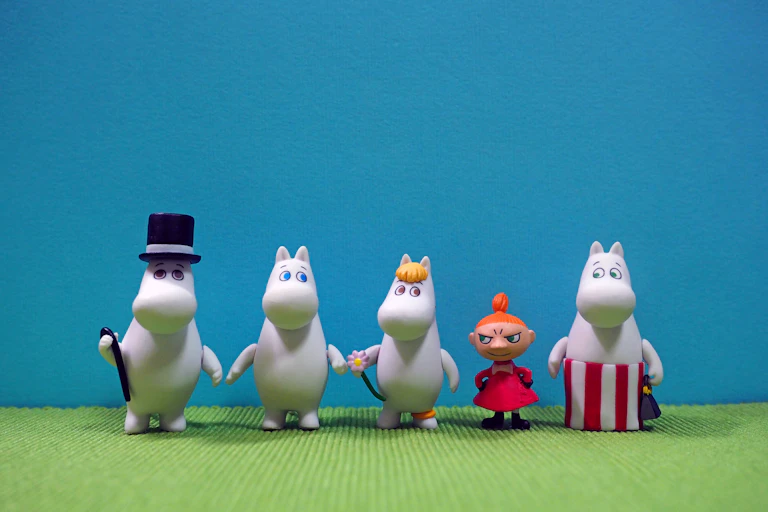 A row of plastic Moomin characters on a green and blue background.