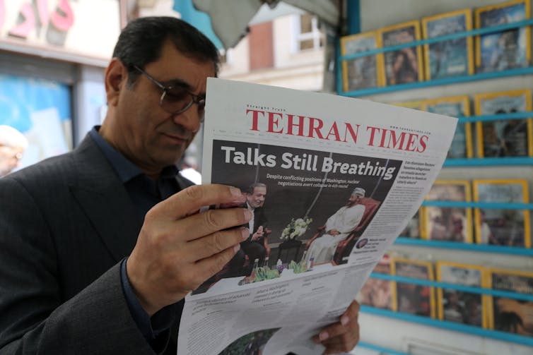 A man holds and reads a newspaper with 'Tehran Times' on the front.