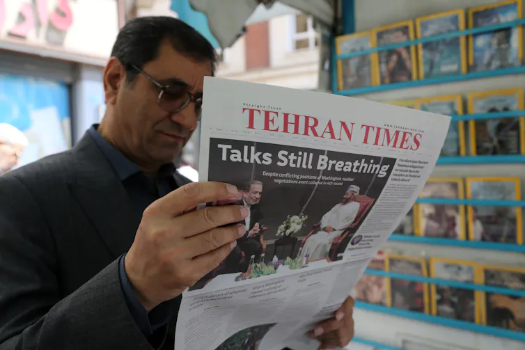 A man holds and reads a newspaper with 'Tehran Times' on the front.