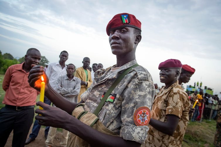 A uniformed soldier holds a candle while people and other soldiers look on.