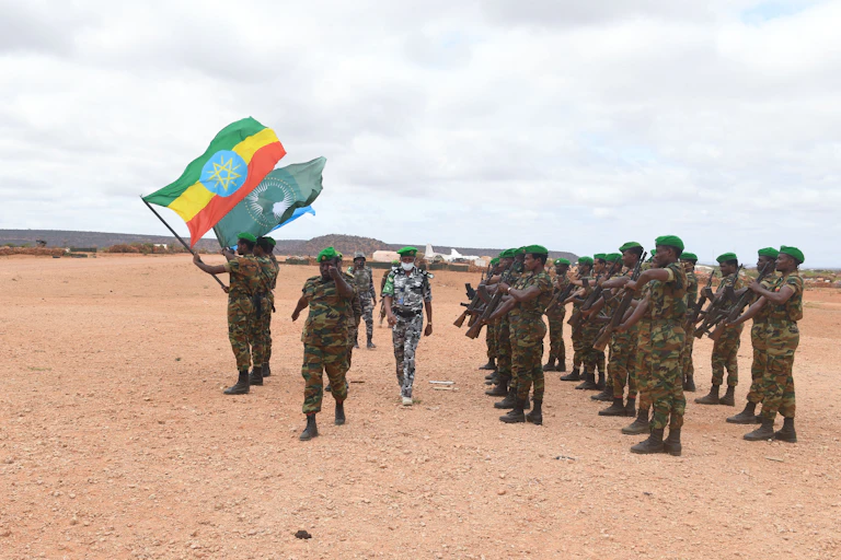 Soldiers standing in formation holding up two flags, one green, the other with red, yellow and red stripes