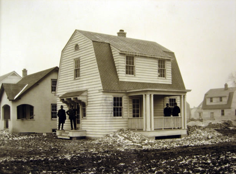 Sepia-toned photograph of a group of men standing in front of a newly-built house.