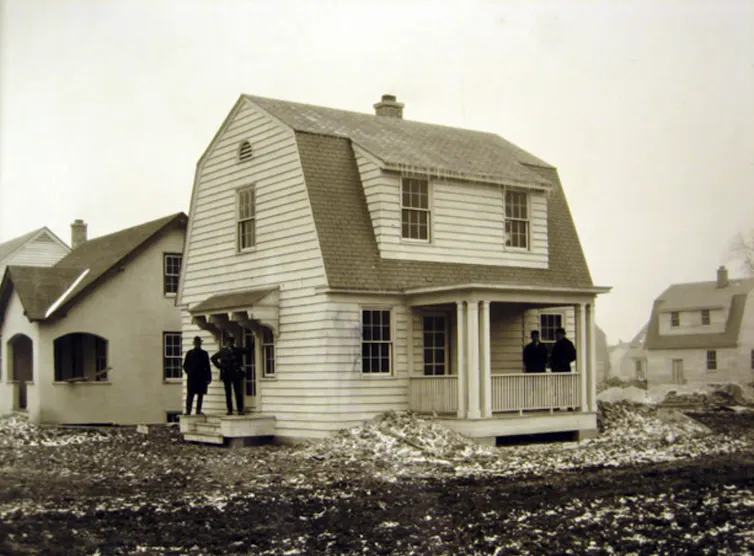 Sepia-toned photograph of a group of men standing in front of a newly-built house.