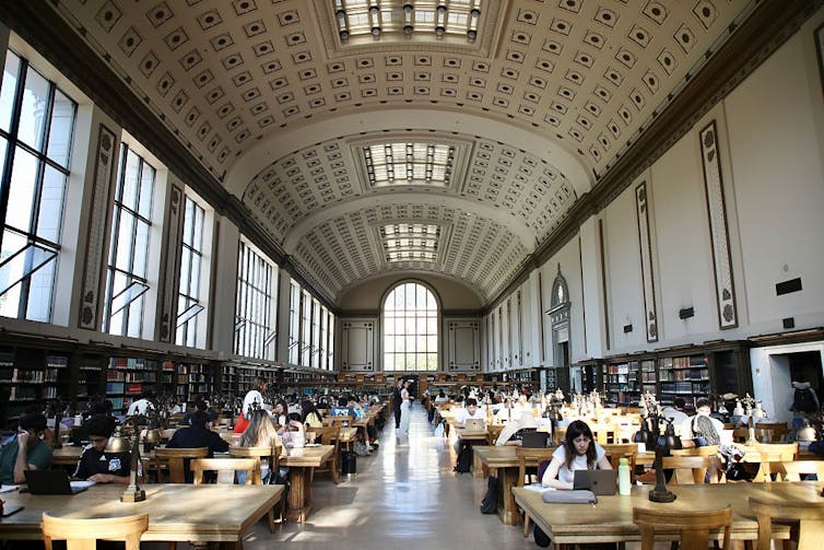 A group of students studying in a large library with high ceilings.