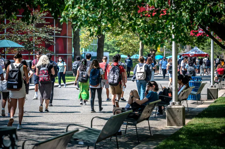 Students with backpacks walk on campus during warm weather.