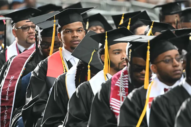 Students dressed in graduation regalia stand in rows.