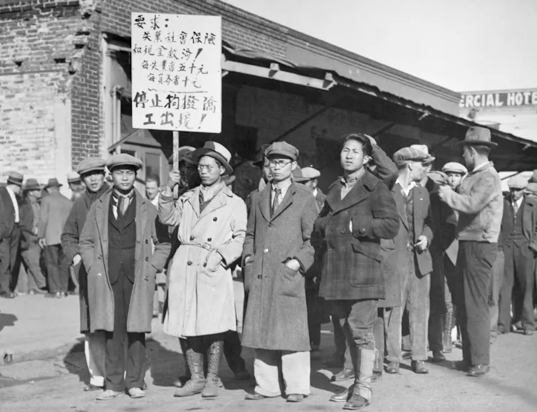 A black-and-white photo of several men of Asian descent holding a banner during a protest.