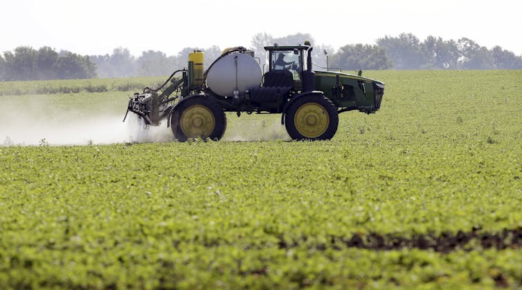 A tractor moves through a field, spraying mist behind it.
