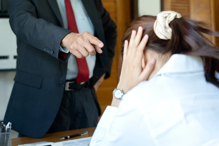 A woman covers her ears with her hands as a man in a suit, seen only from the neck down, points a finger at her
