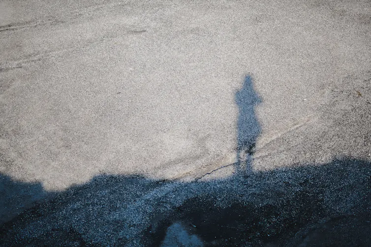 The shadow of a small figure on grey pavement.