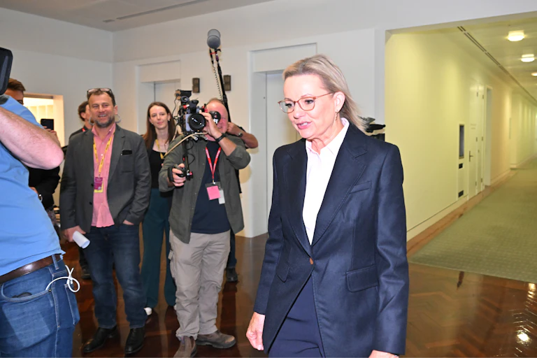 Sussan Ley wearing a tailored suit with reporters and a camera crew in the background.