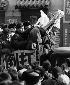 A black and white photo of two men in long, paper dunces' hats amid of a crowd of people.