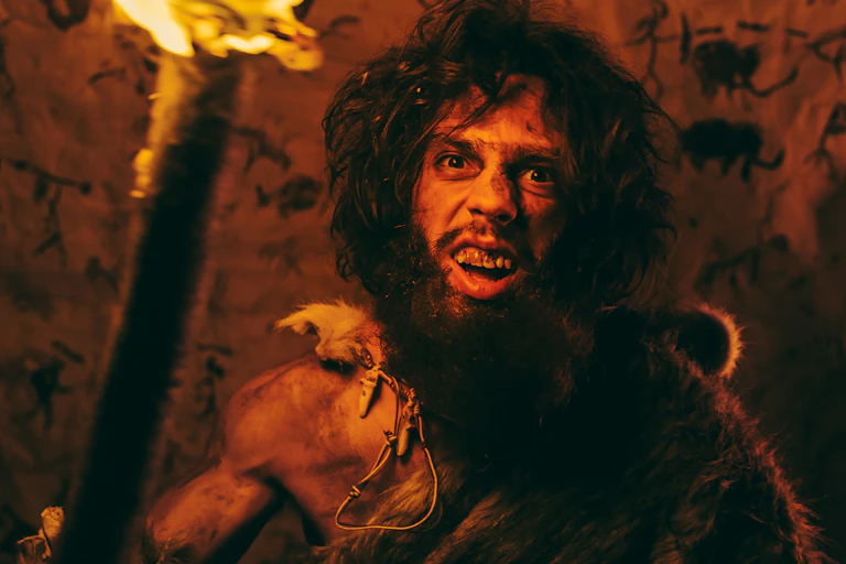 Portrait of Primeval Caveman Wearing Animal Skin Standing in His Cave At Night, Holding Torch