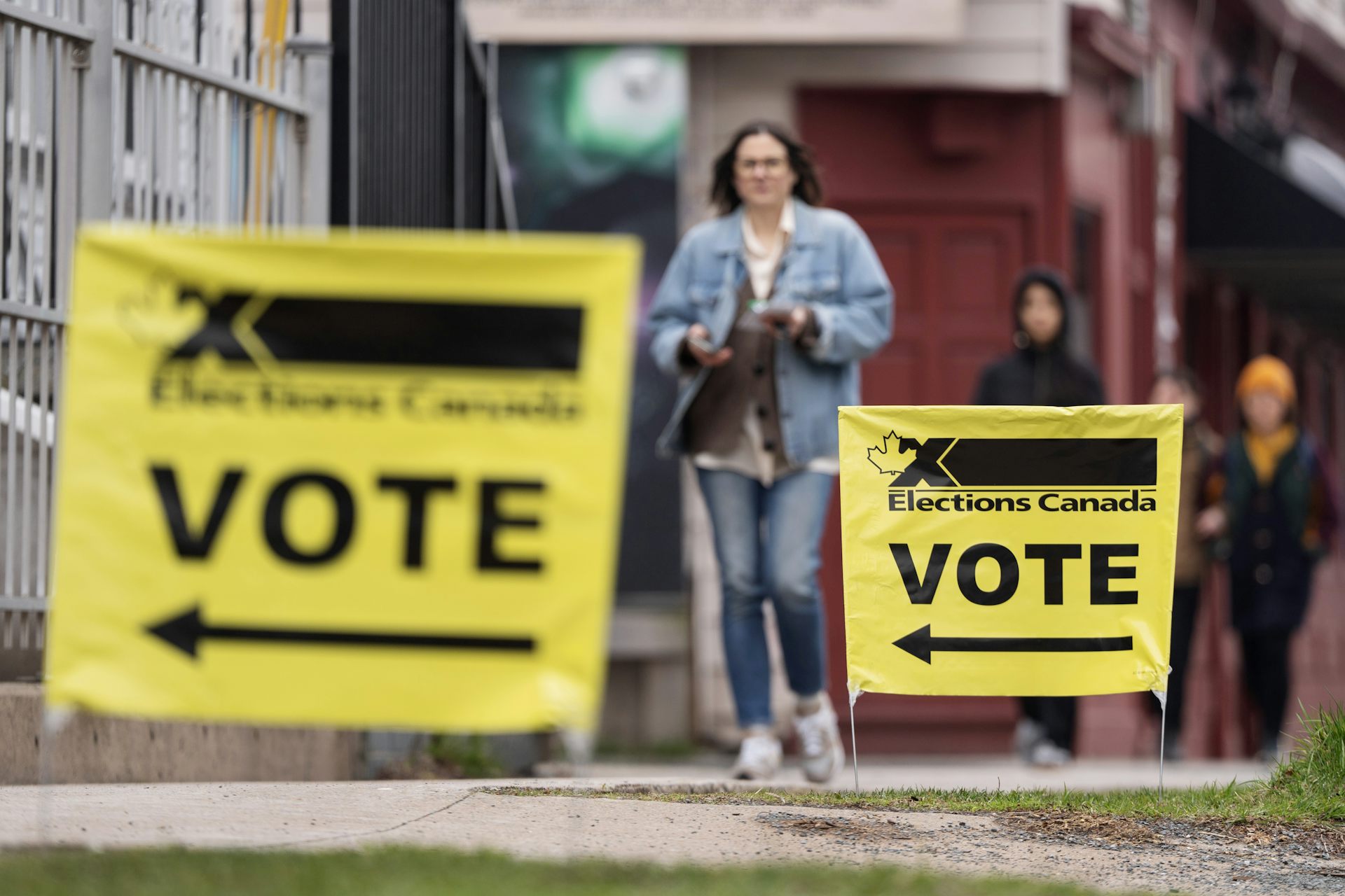 Elecciones se pueden ver letreros canadienses en ambos lados de una mujer con jeans y chaquetas de jean mientras camina hacia la estación de votación.