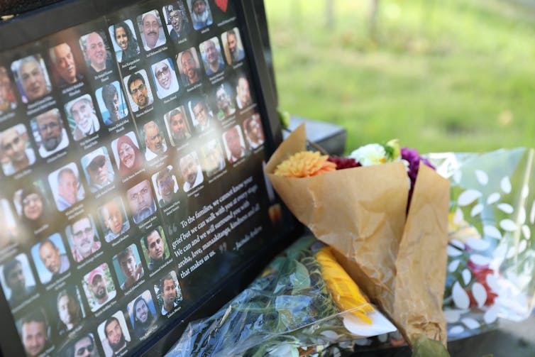 Flowers are laid next to a board showing the names and faces of people
