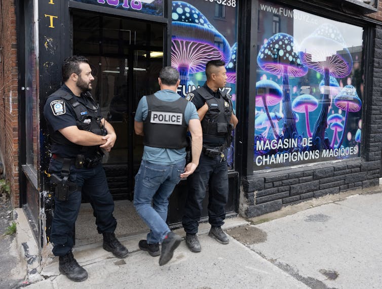 Tres hombres con uniforme negro frente a las tiendas con coloridos champiñones en la ventana