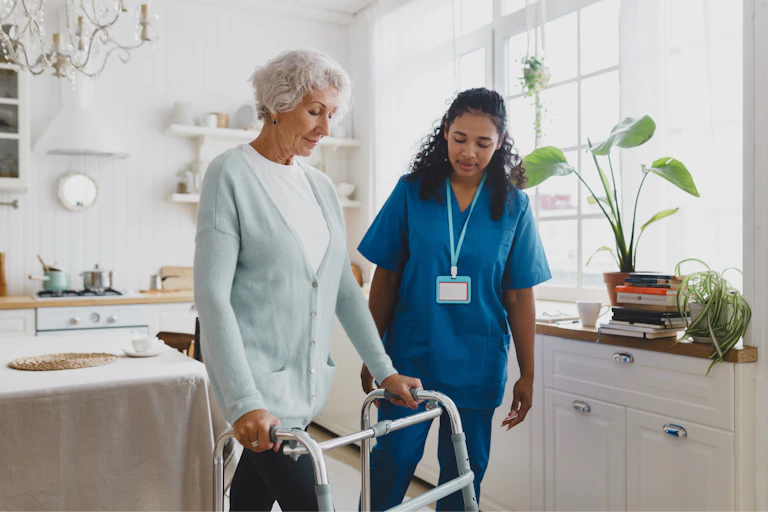 care worker helping older woman walking with a zimmer frame.