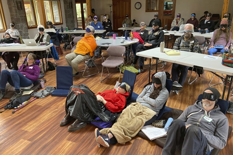 El surgimiento del capitalismo psicodélico: ¿trabajar más duro y ser feliz por ello? 1 La gente se encuentra o la mitad se sentó con máscaras para los ojos. Muchos también tienen mantas. Están en colocar el aula con mesas comunes.