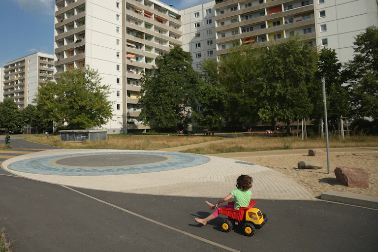 A child plays alone next to a large apartment complex that is otherwise empty.