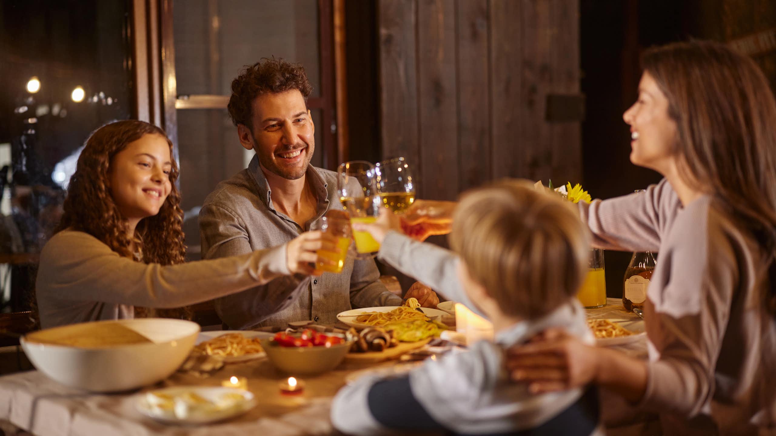 White family with tween children looking happy at the dinner table and raising their glasses in a toast