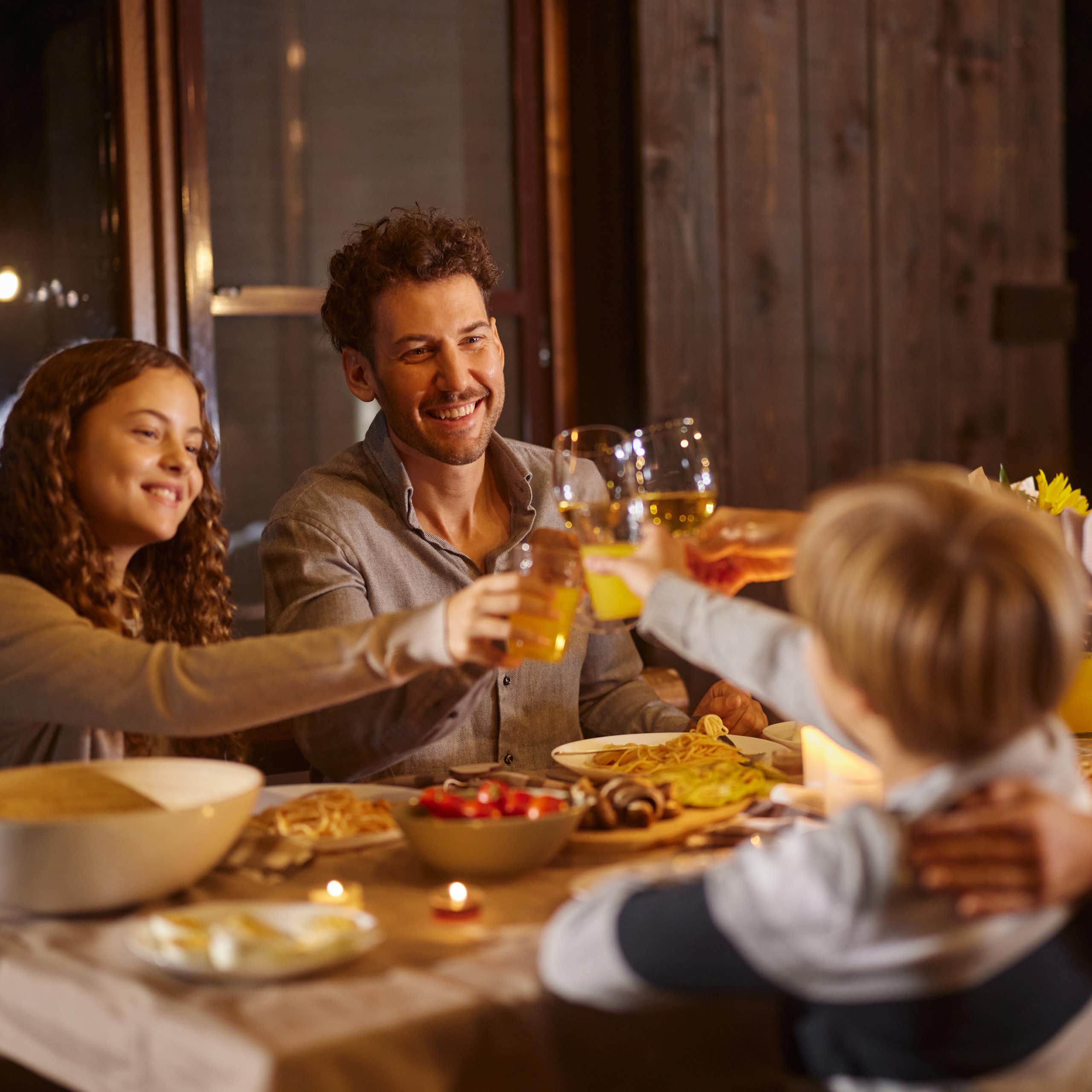 White family with tween children looking happy at the dinner table and raising their glasses in a toast
