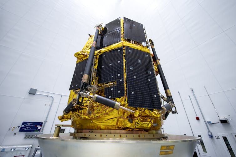 A lander – which looks like a large box with metal sides – on a platform in a white room.