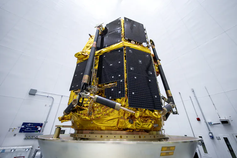 A lander – which looks like a large box with metal sides – on a platform in a white room.