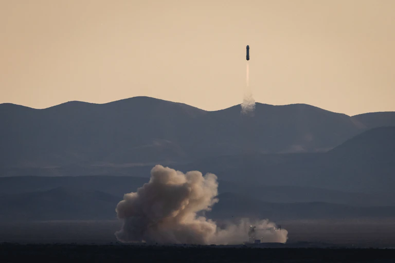 A rocket launching with a plume of smoke in front of a mountain ridge.