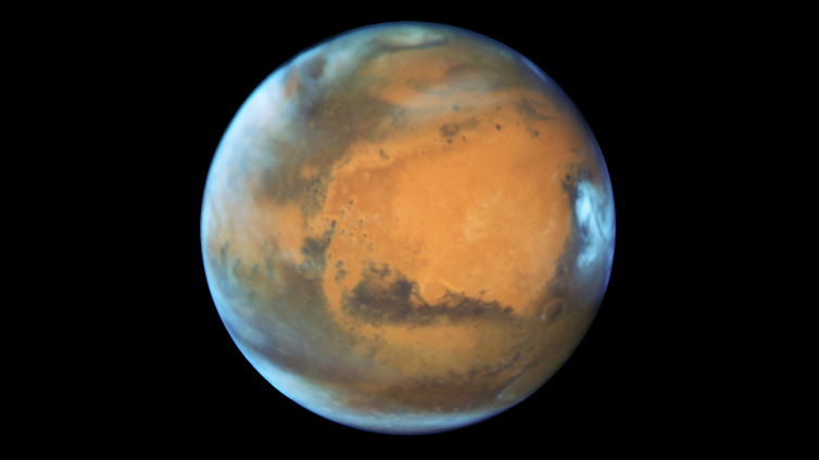 A photo of Mars from space. It looks reddish brown in color, with white clouds at the poles.