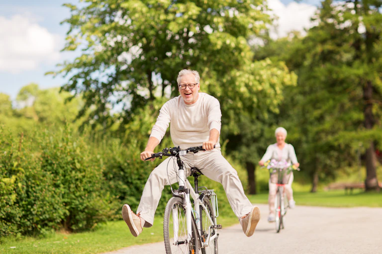 Happy senior couple riding bicycles through park in summer