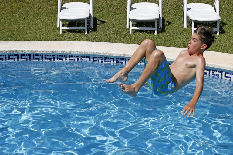 Leading with his back, a boy jumps in a pool.
