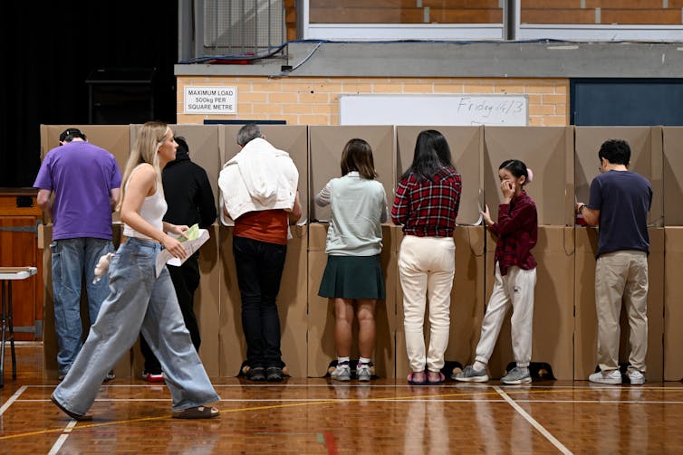 A young voter walks past a line of people filling in ballot papers