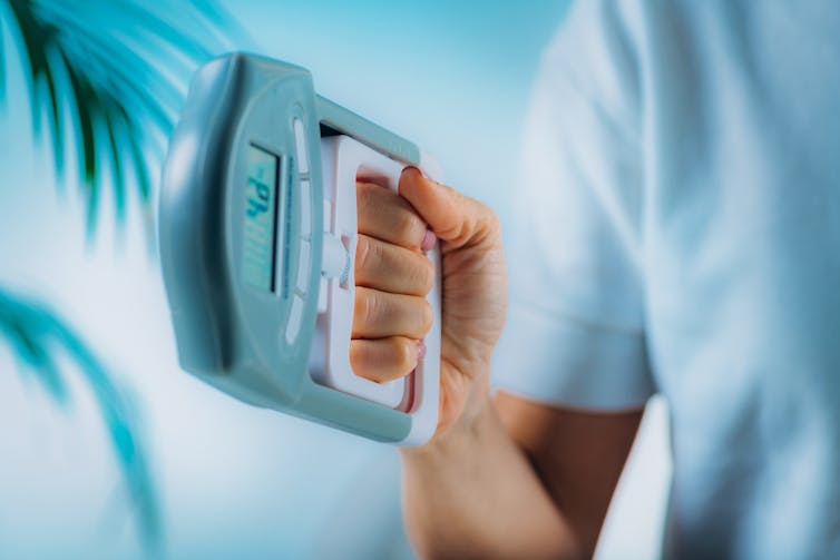 The person squeezes the dynanometer with his hand to measure the strength of adhesion.