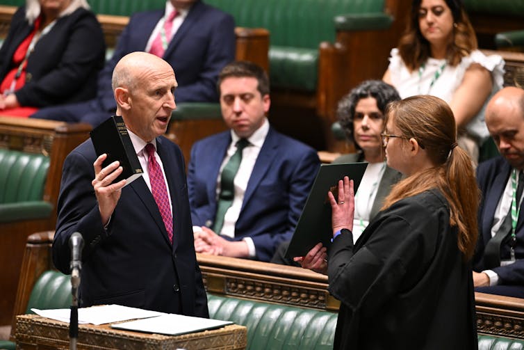 John Healey being sworn in in the House of Commons chamber, holding up a bible.