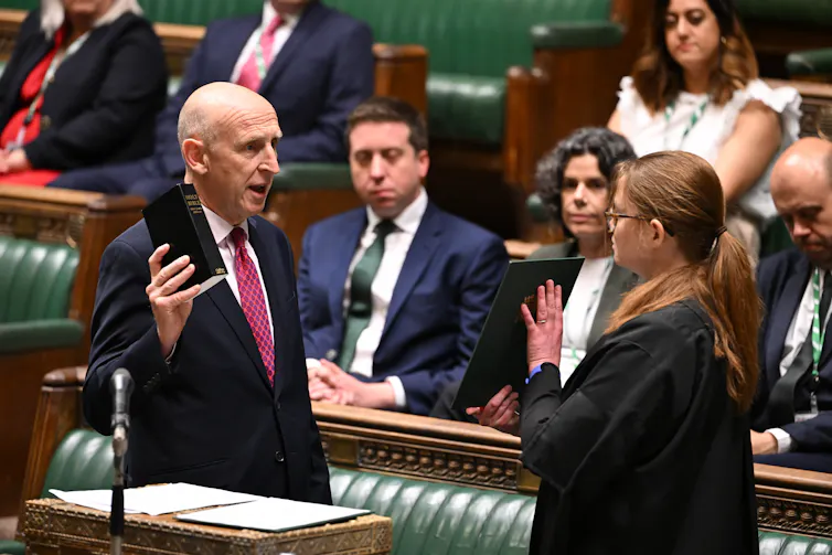 John Healey being sworn in in the House of Commons chamber, holding up a bible.