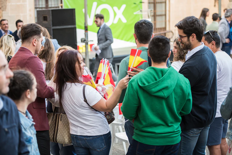 Una chica reparte banderas de España a los asistentes de un mitin de Vox