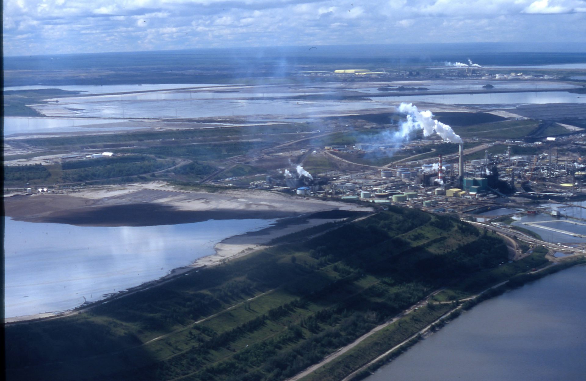 Une vue aérienne montre deux installations d'exploitation des sables bitumineux dans un vaste paysage.