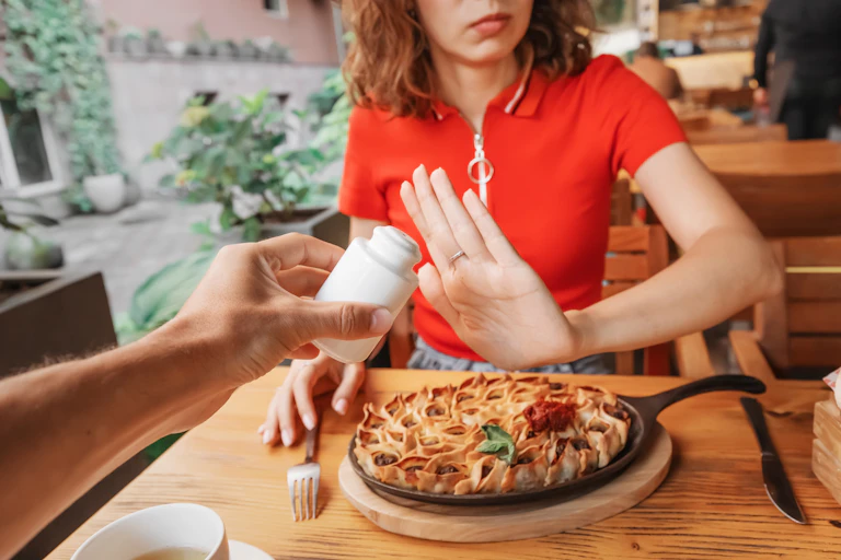 Une femme à table refuse la salière qu'on lui tend.