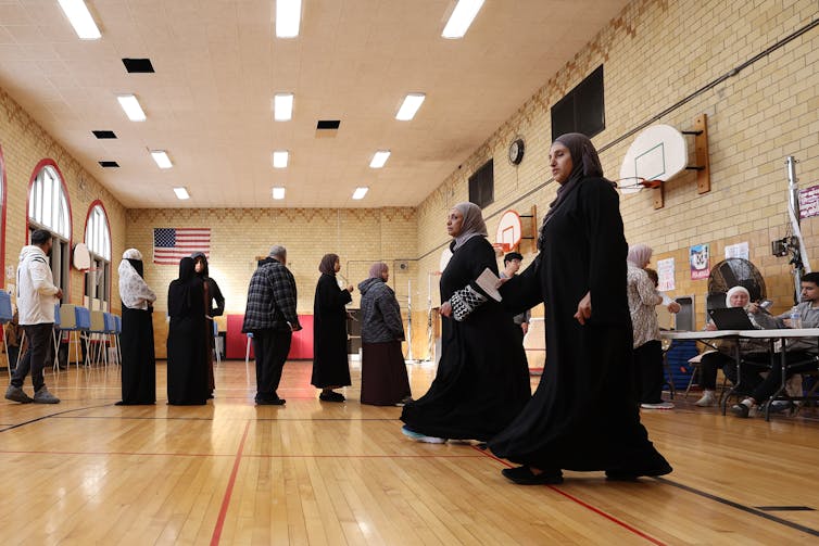 Las mujeres en hijabs están esperando en la fila para votar en el gimnasio escolar.