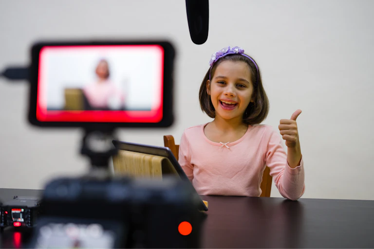 A young girl is seen on a video screen smiling and gesturing to a phone camera.