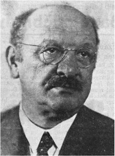 Black and white photograph of a man with a mustache wearing wire-rimmed glasses