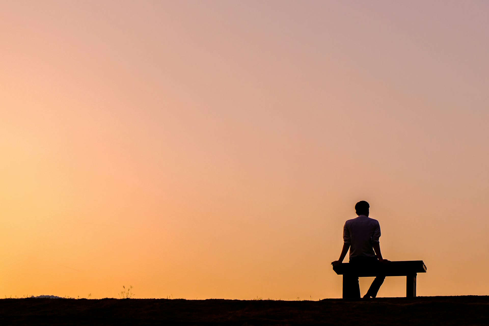Silhouette of a person sitting on a bench against a sunset sky