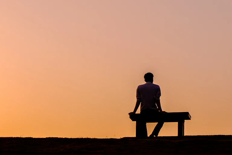 Silhouette of a person sitting on a bench against a sunset sky